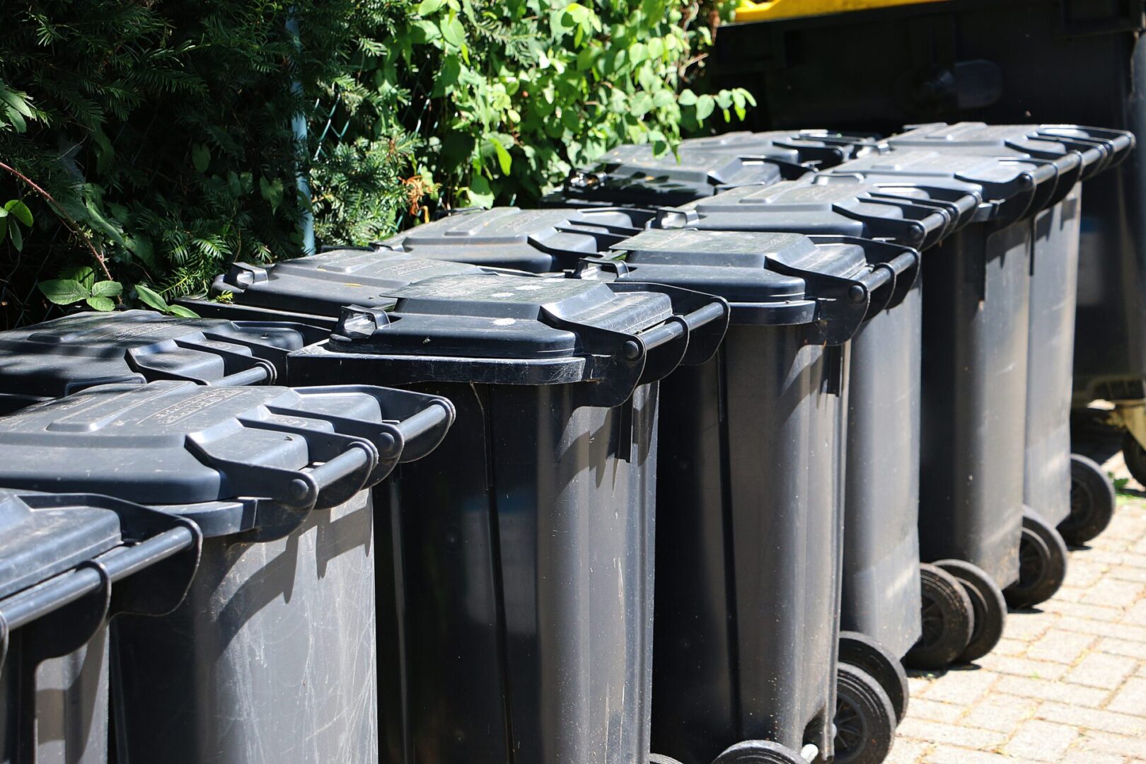 A row of black garbage cans sitting next to each other.