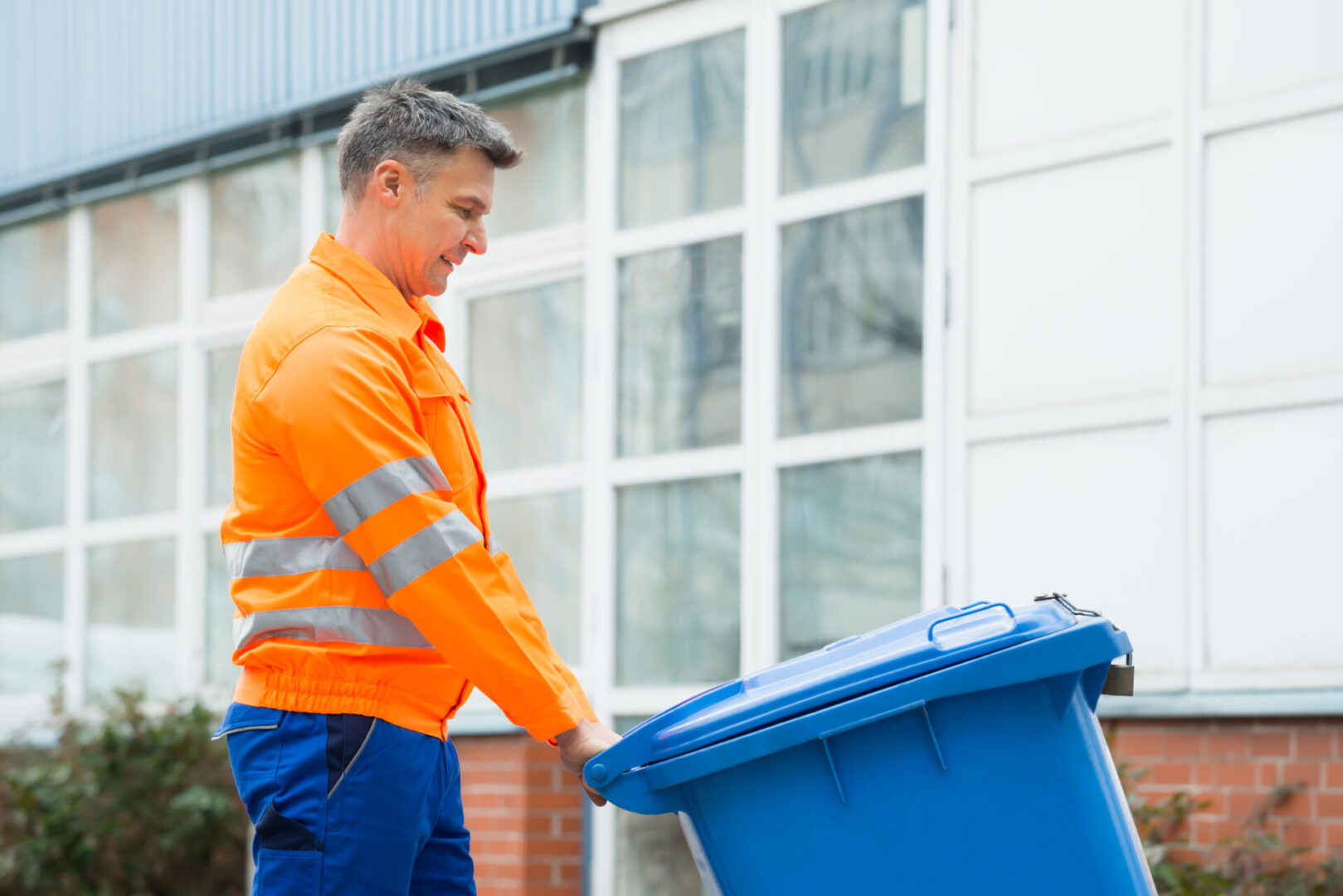 A man in an orange jacket is loading trash.